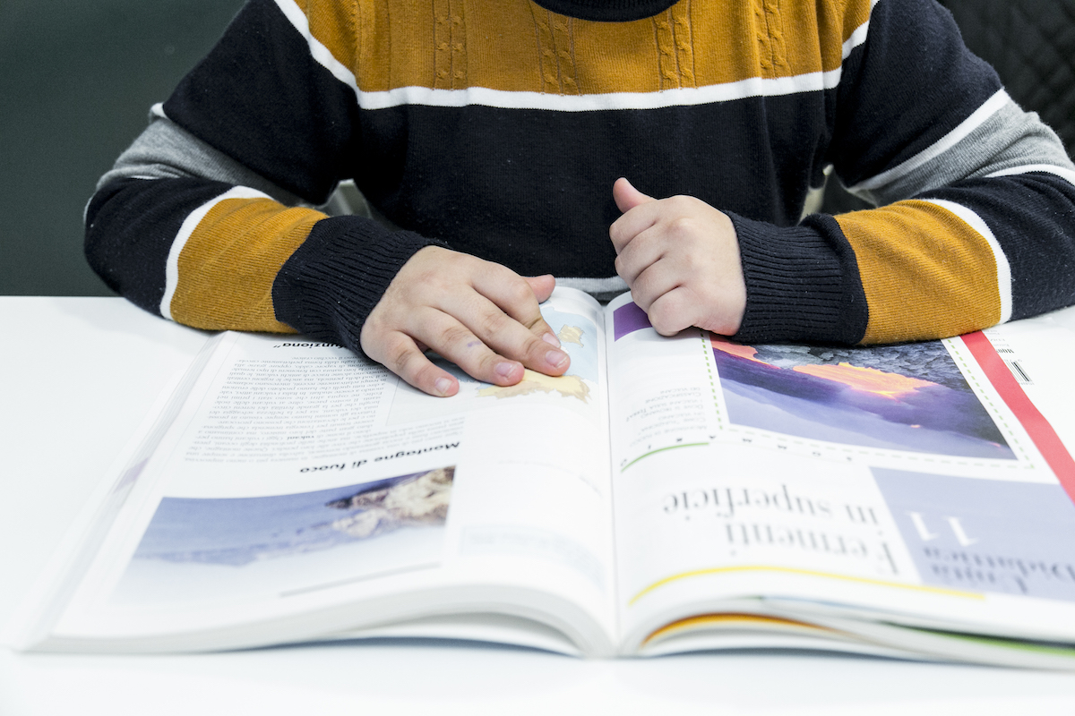 Primo piano di bambino con un maglione a righe che studia su un libro